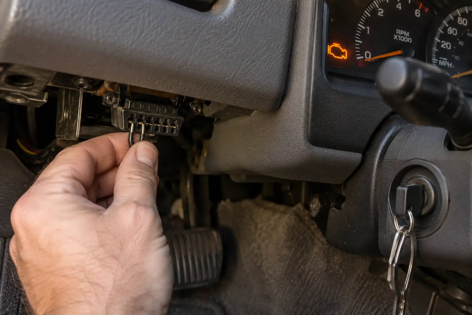 A hand inserting a jumper wire into an old under-dash diagnostic connector while the check engine light flashes on the dashboard.