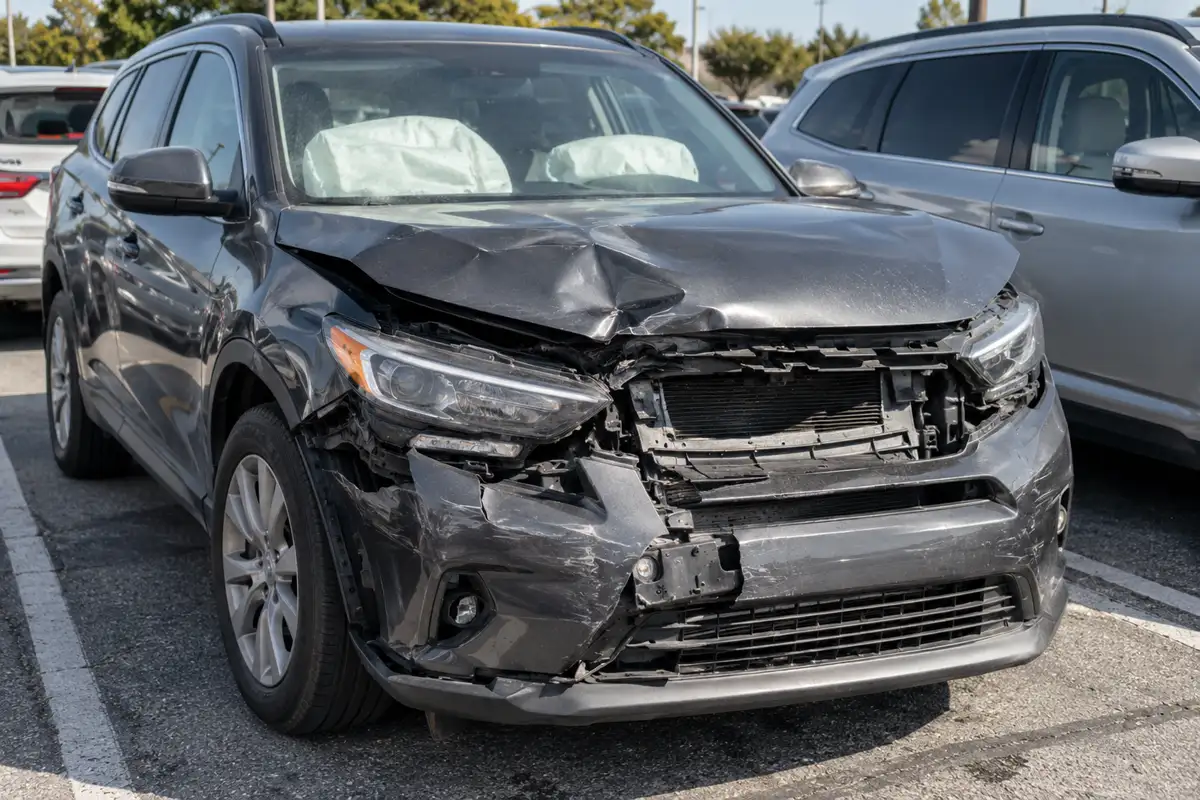 Gray SUV with damaged front bumper and deployed airbags after a collision in a parking lot.