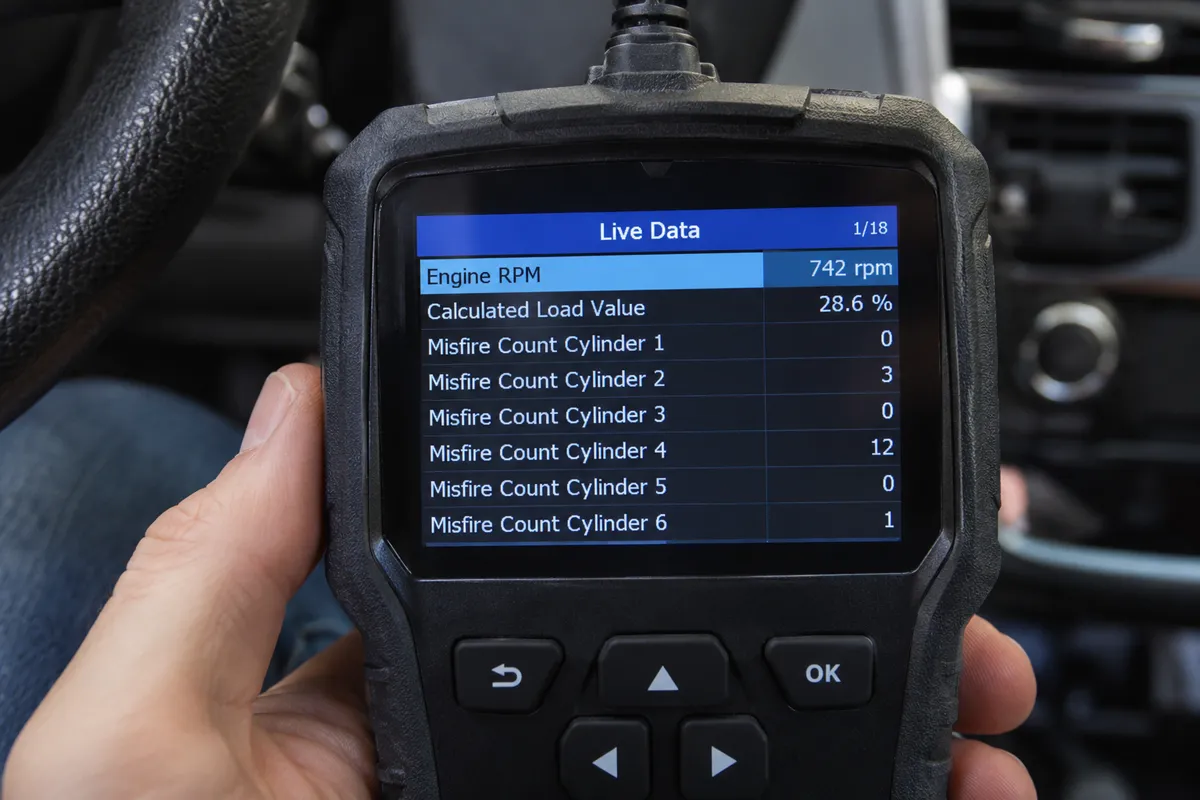 Close-up of a handheld OBD2 scanner showing engine RPM, load, and individual cylinder misfire counters.