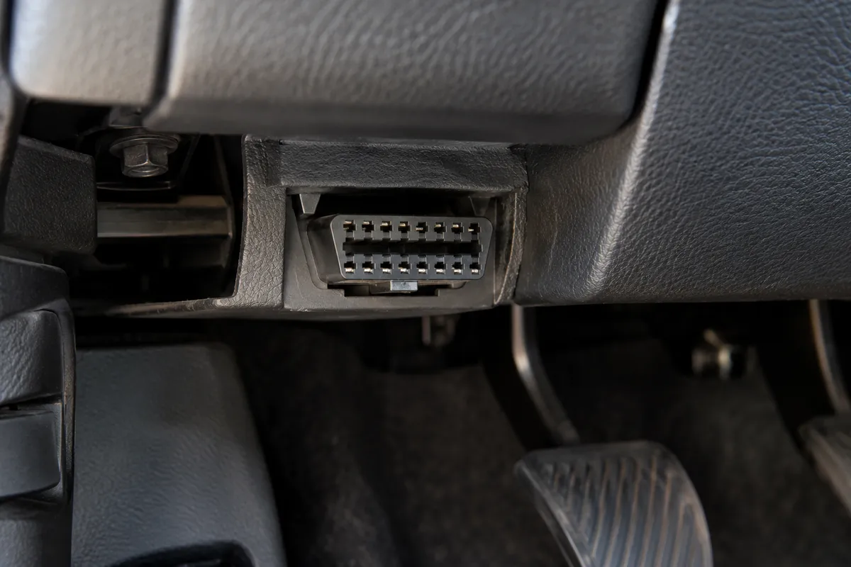 Close-up of the 16-pin trapezoidal OBD2 diagnostic link connector beneath a car dashboard.